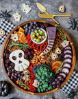 Halloween-themed charcuterie board with various foods and decorative elements on a gray surface.