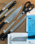 Set of knives and a pair of scissors on a cardboard surface with packaging materials.