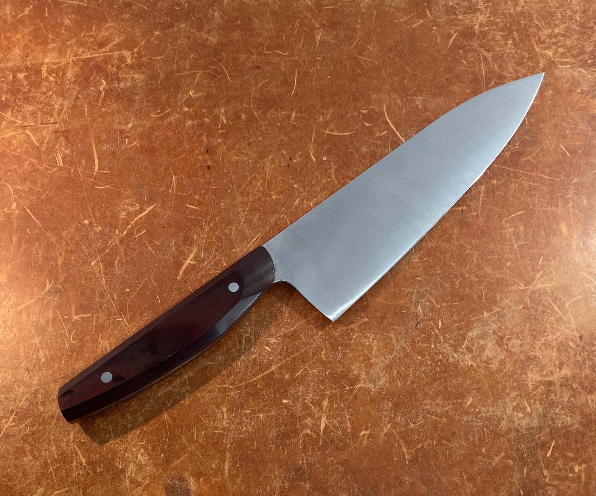 Chef&#39;s knife with a brown handle on a brown surface