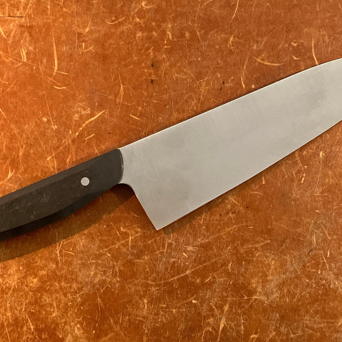 Chef's knife with a black handle on a brown surface