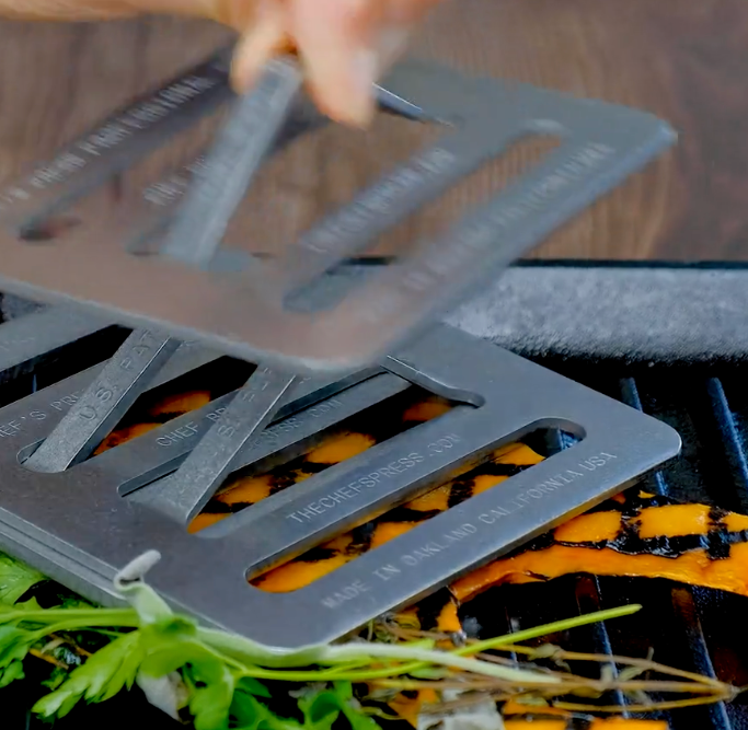 Metal grill chefs press being used on a grill with vegetables