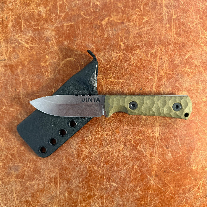Knife with green handle and black sheath on a brown surface uinta