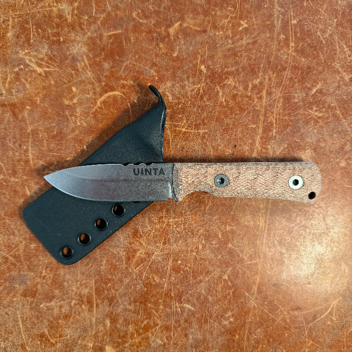 Knife with wooden handle and black sheath on a brown textured surface uinta