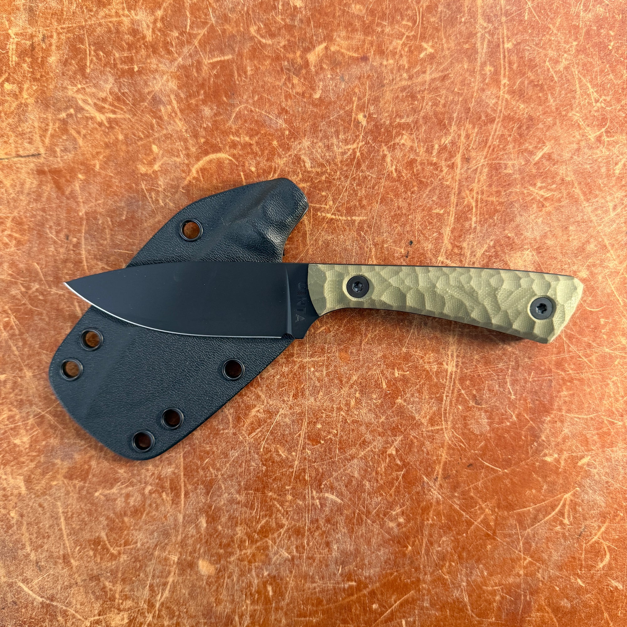 Knife with a black sheath on a brown leather surface Uinta