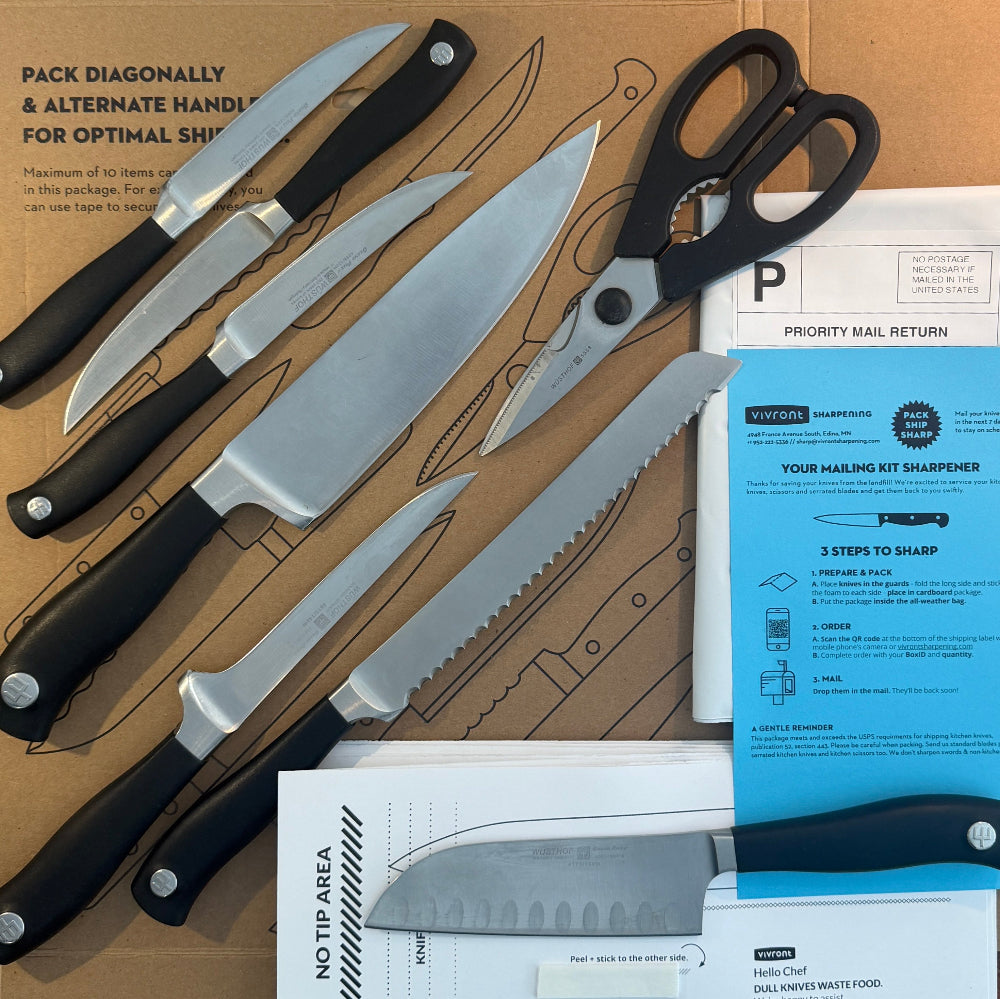 Set of knives and a pair of scissors on a cardboard surface with packaging materials.