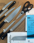 Set of knives and a pair of scissors on a cardboard surface with packaging materials.